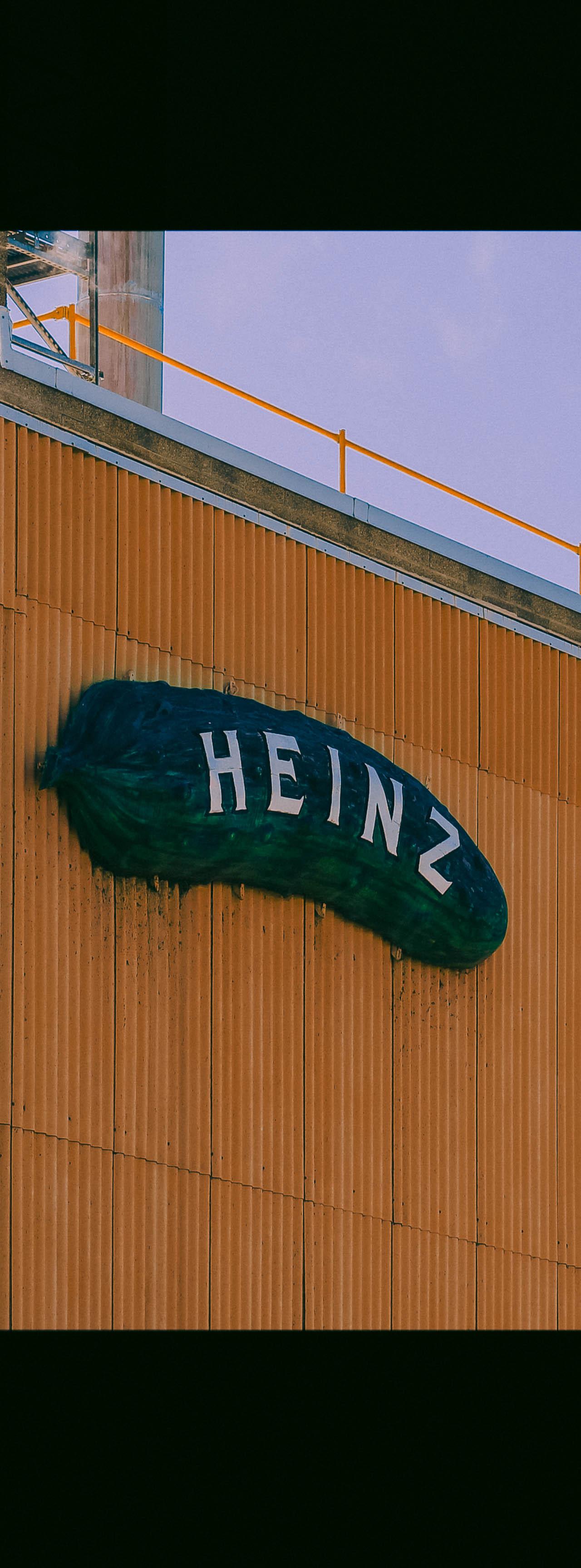 A low-angle shot of an industrial building. The main wall is covered in orange corrugated metal, while a brick wall on the left corner emits a wisp of steam.